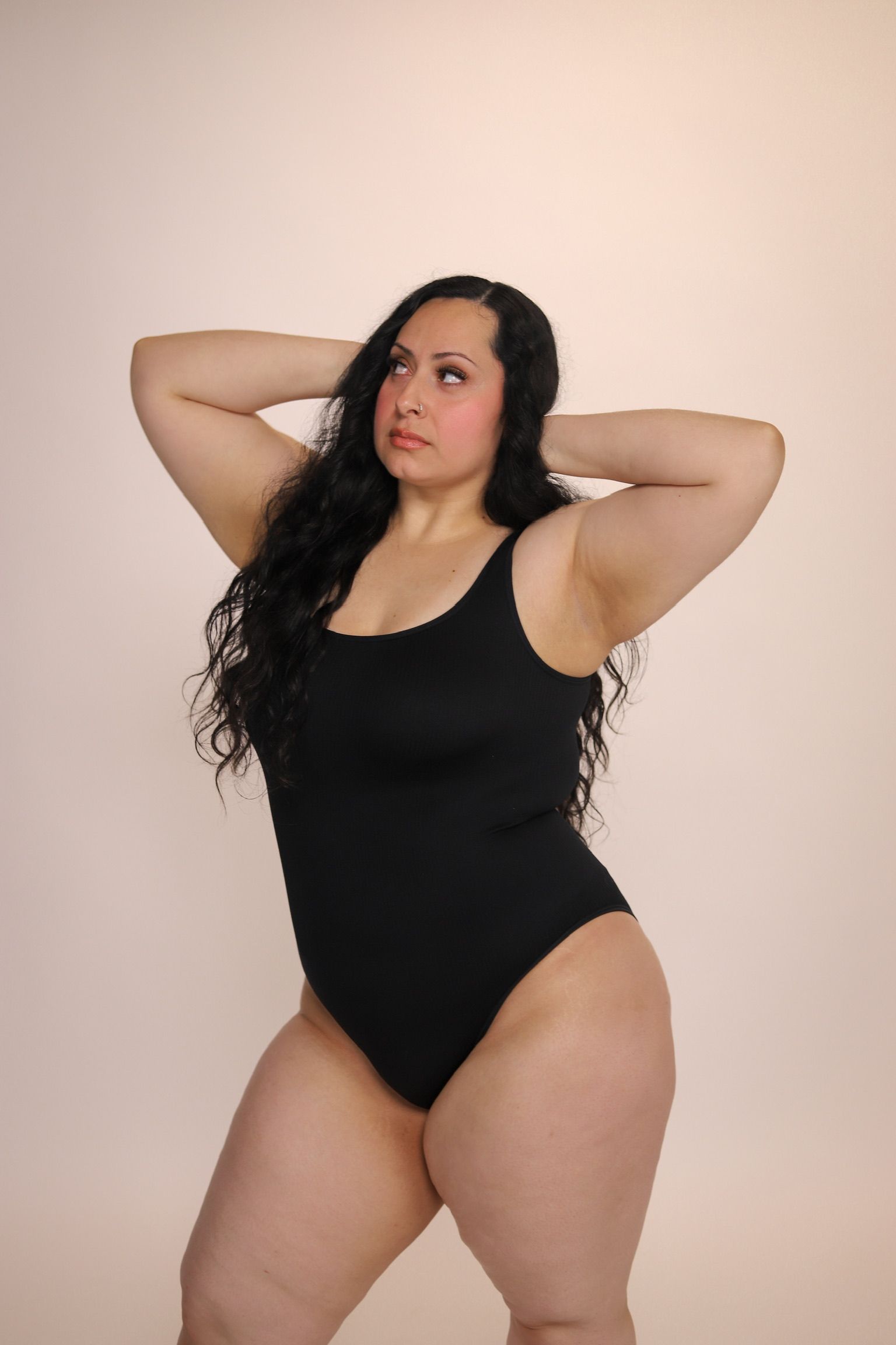 Woman raises arm, hand touching armpit; light skin, neutral background.