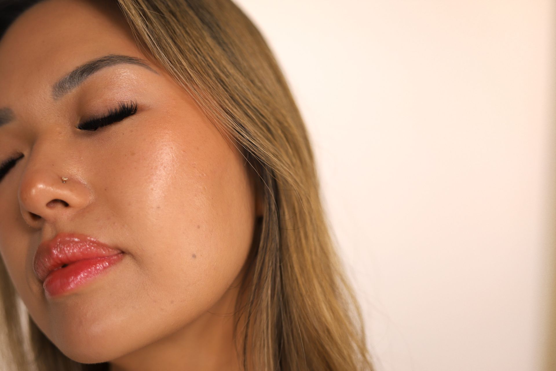 Woman with braided hair smiling, hand on chin, pink background.