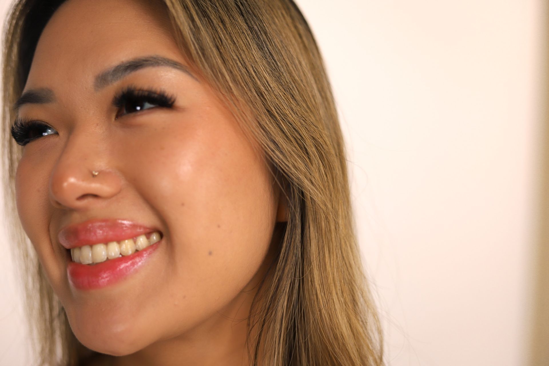 Smiling person with long eyelashes, light hair, and a nose piercing.