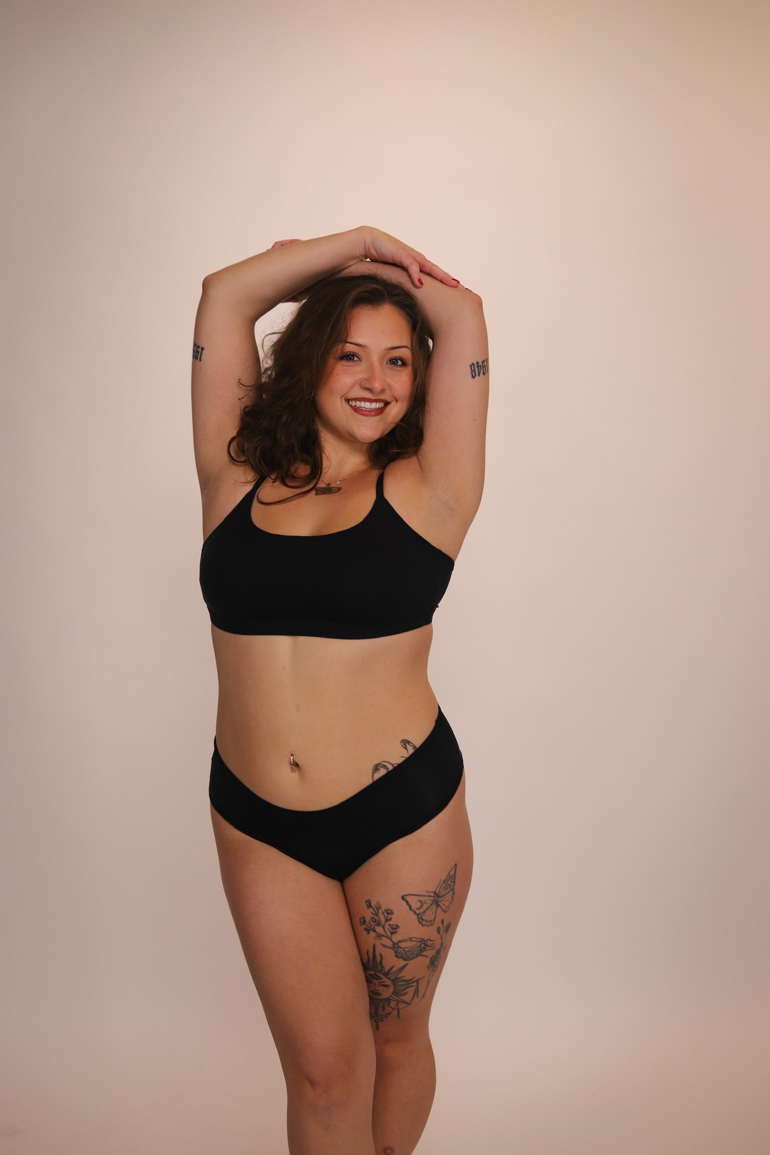 Woman in white lingerie against a pink background, arms raised near head.