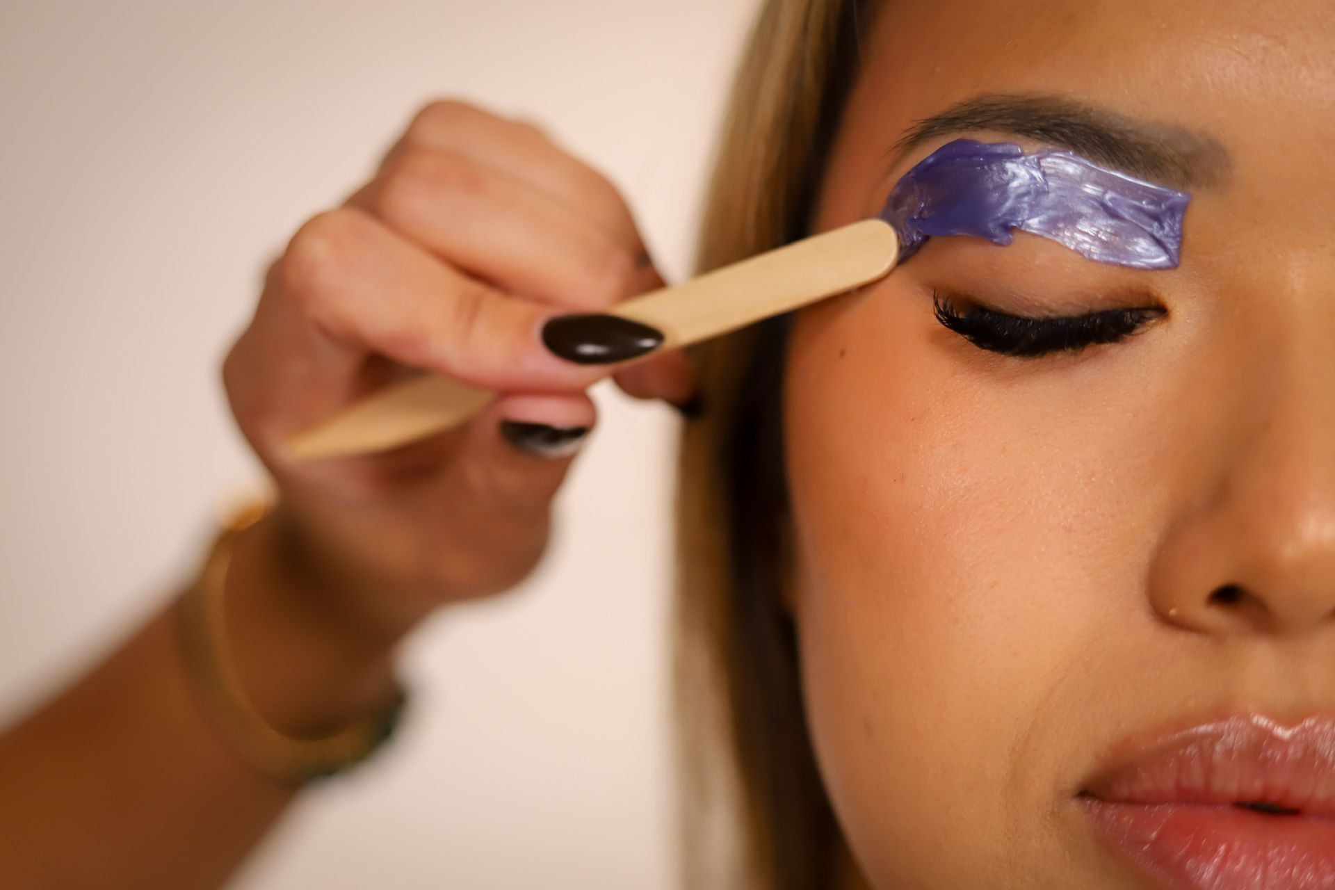 Close-up of eye and eyebrow being brushed with a pink spoolie. The eye is blue-green.