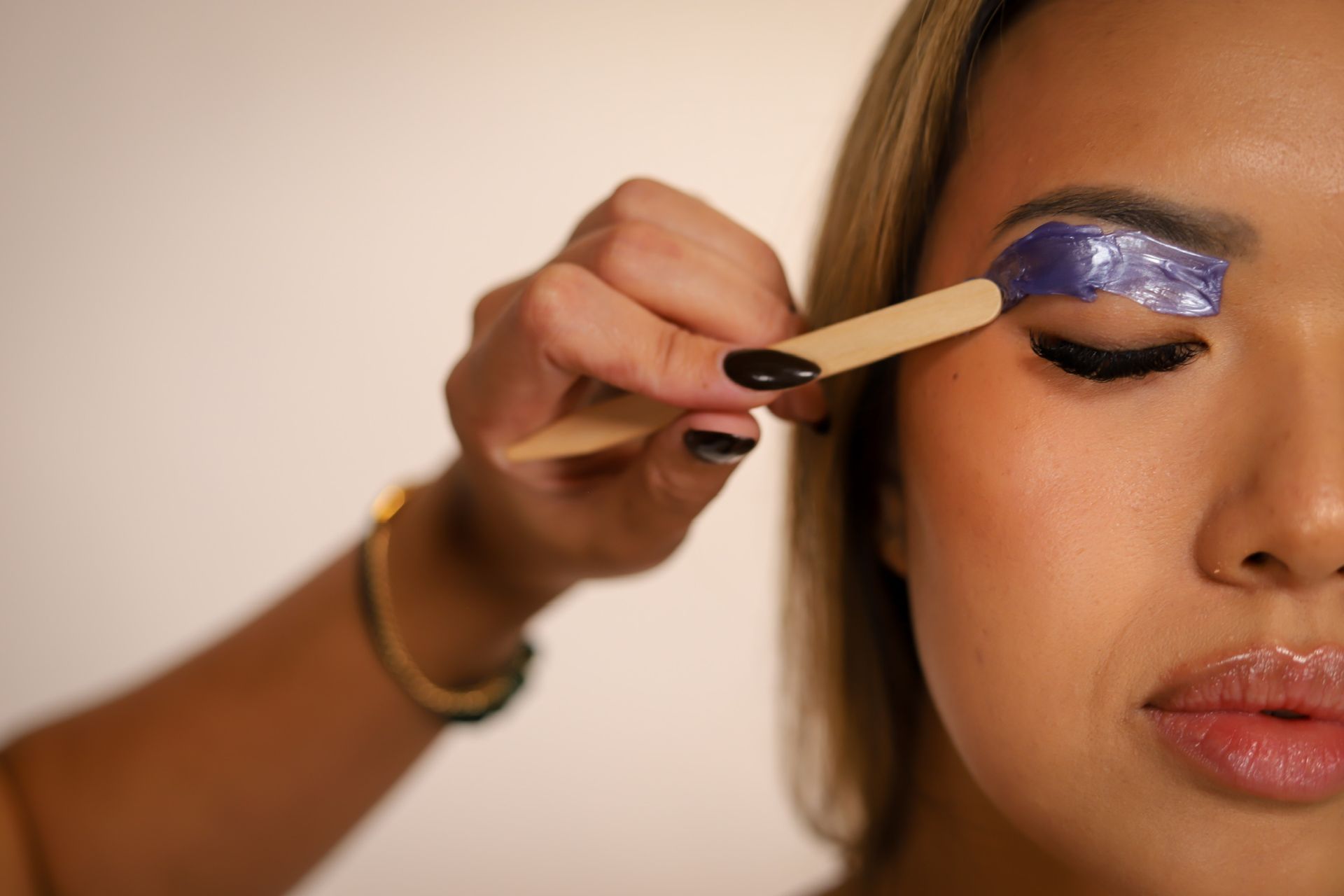 Someone applies brow tint with a small tool to a person's eyebrow in a salon.