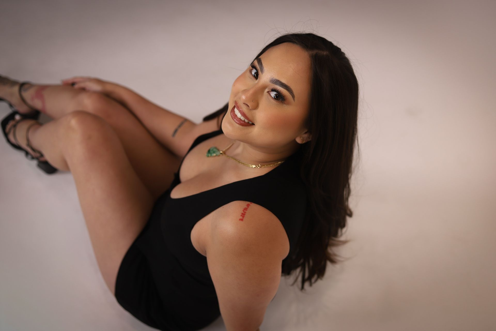 Makeup artist applying eyeshadow to a client's closed eye. Both are in black shirts, against a light backdrop.