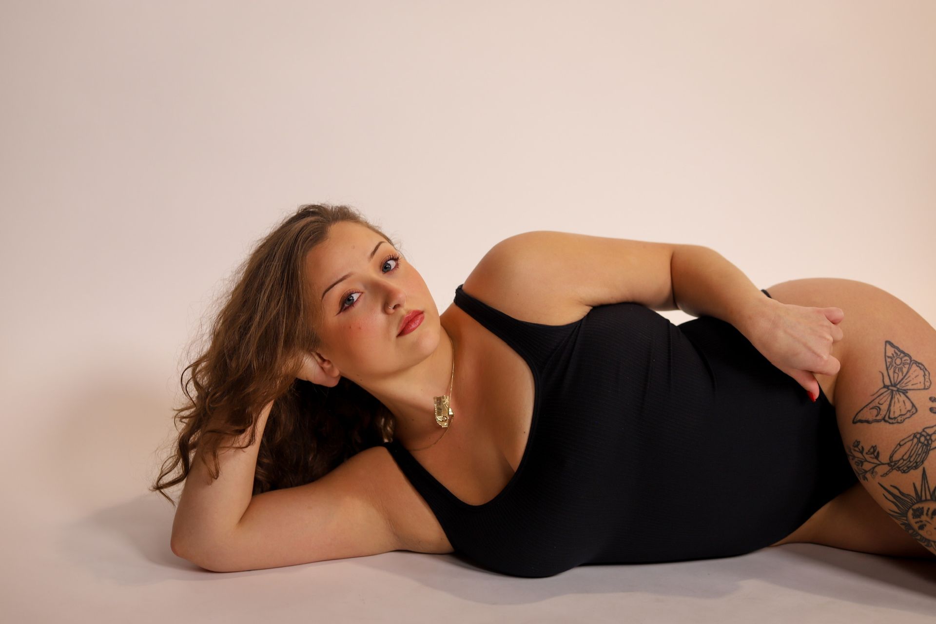 Woman in beige lingerie poses against a yellow backdrop, arms raised.