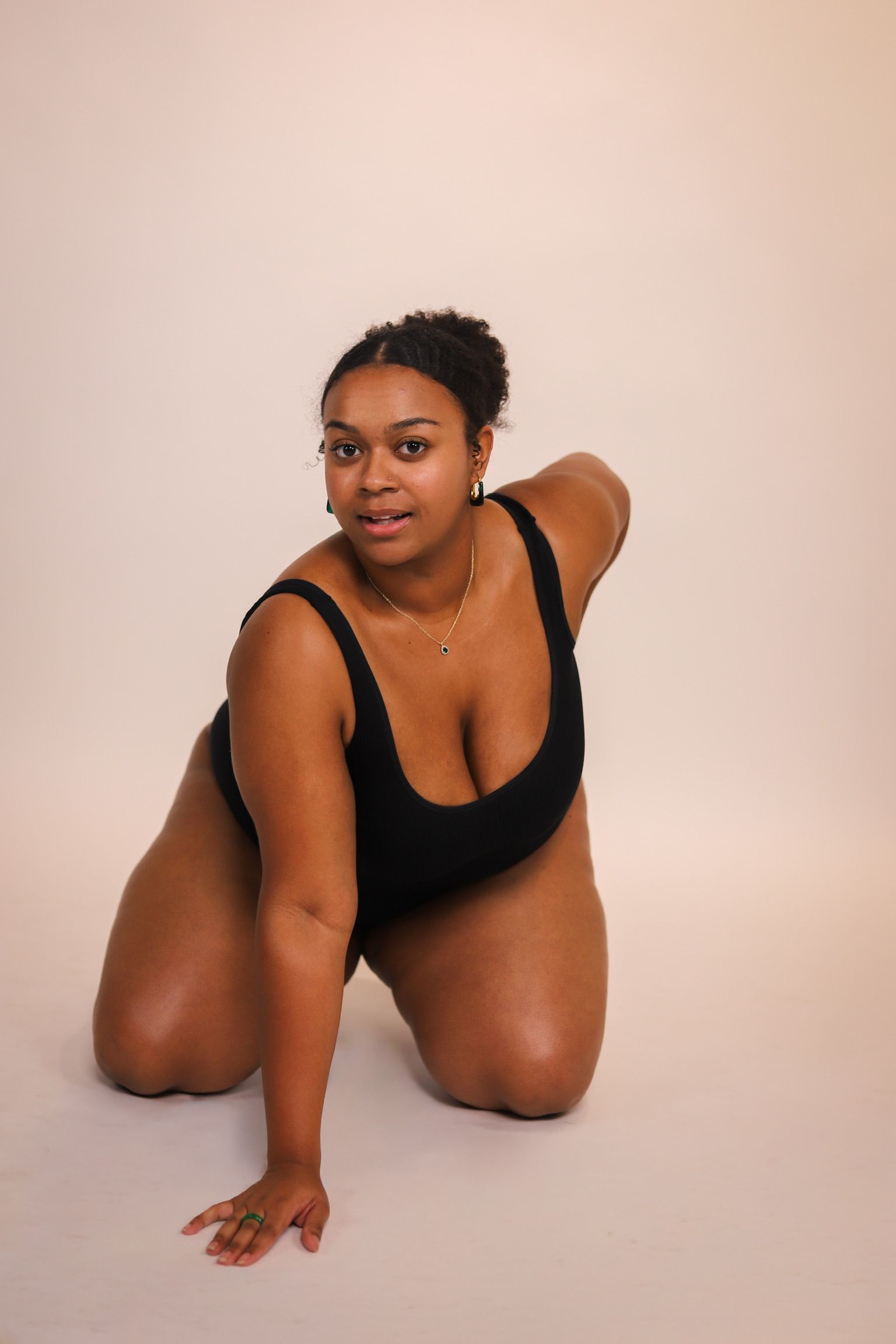 Woman with arm raised, touching underarm; wearing a white strapless top.