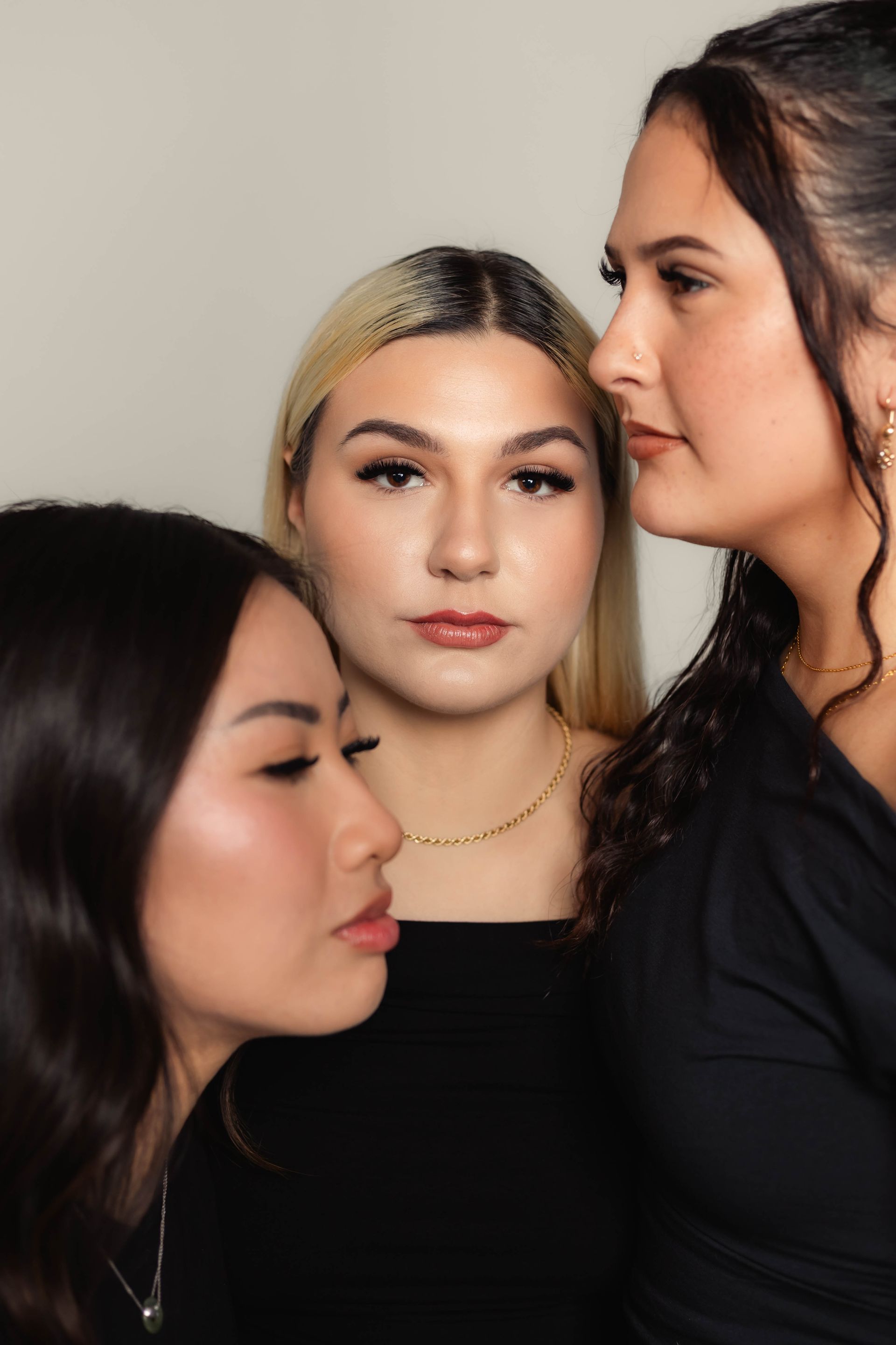 Three women, posing closely together, lit with neutral background.