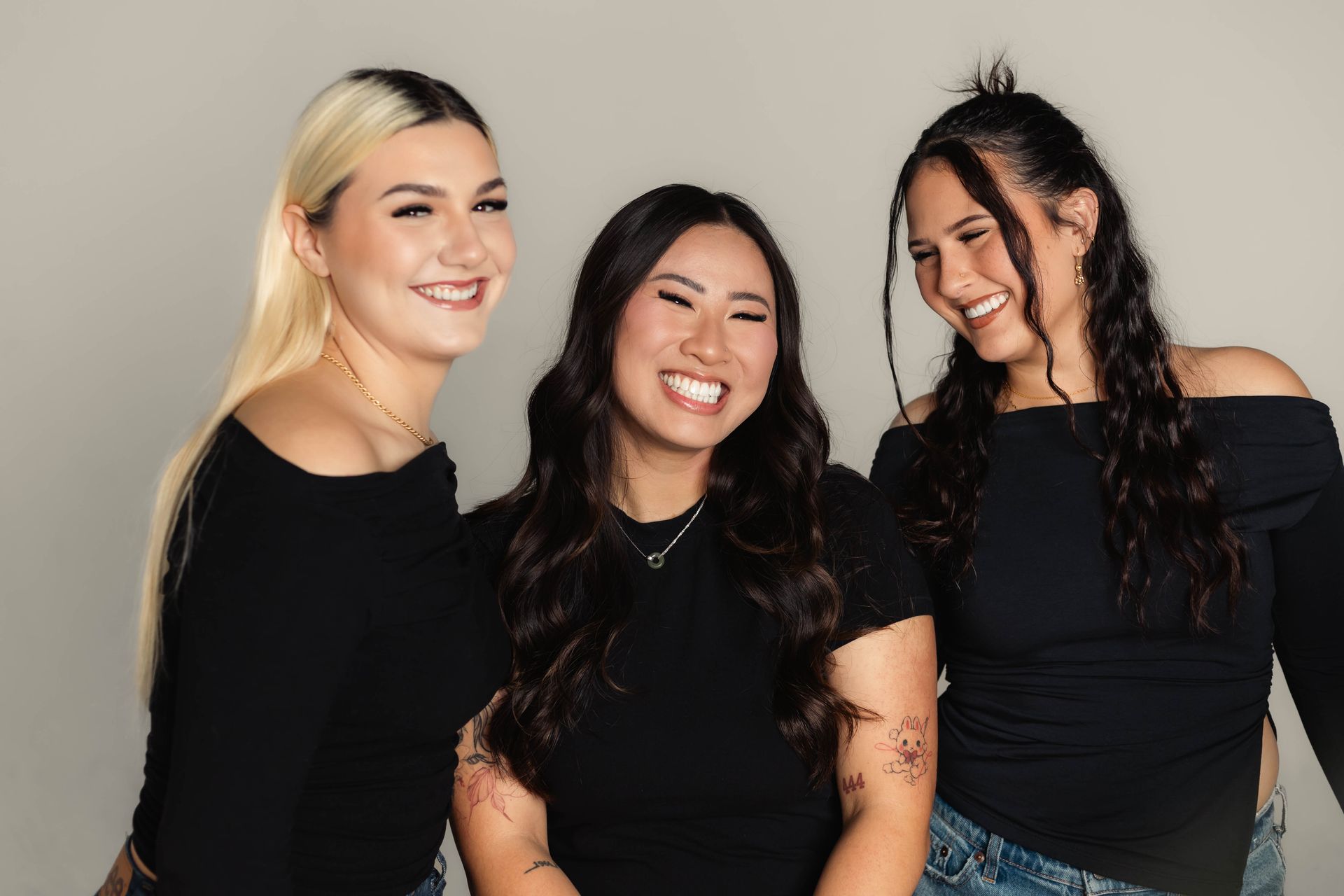 Three smiling people in black tops, posing together against a neutral background.