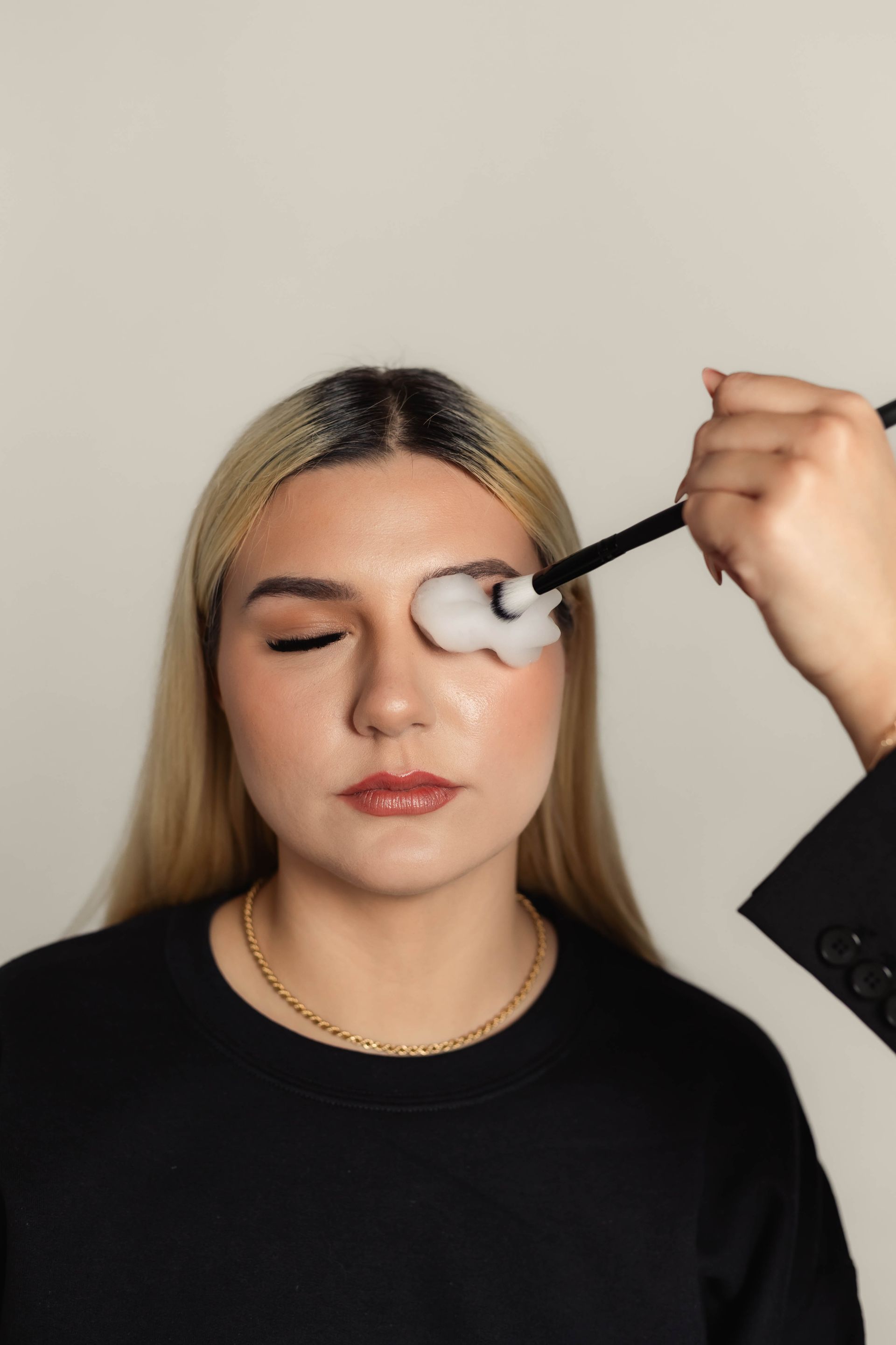 Person with closed eyes has makeup applied to her eyelid with a brush.