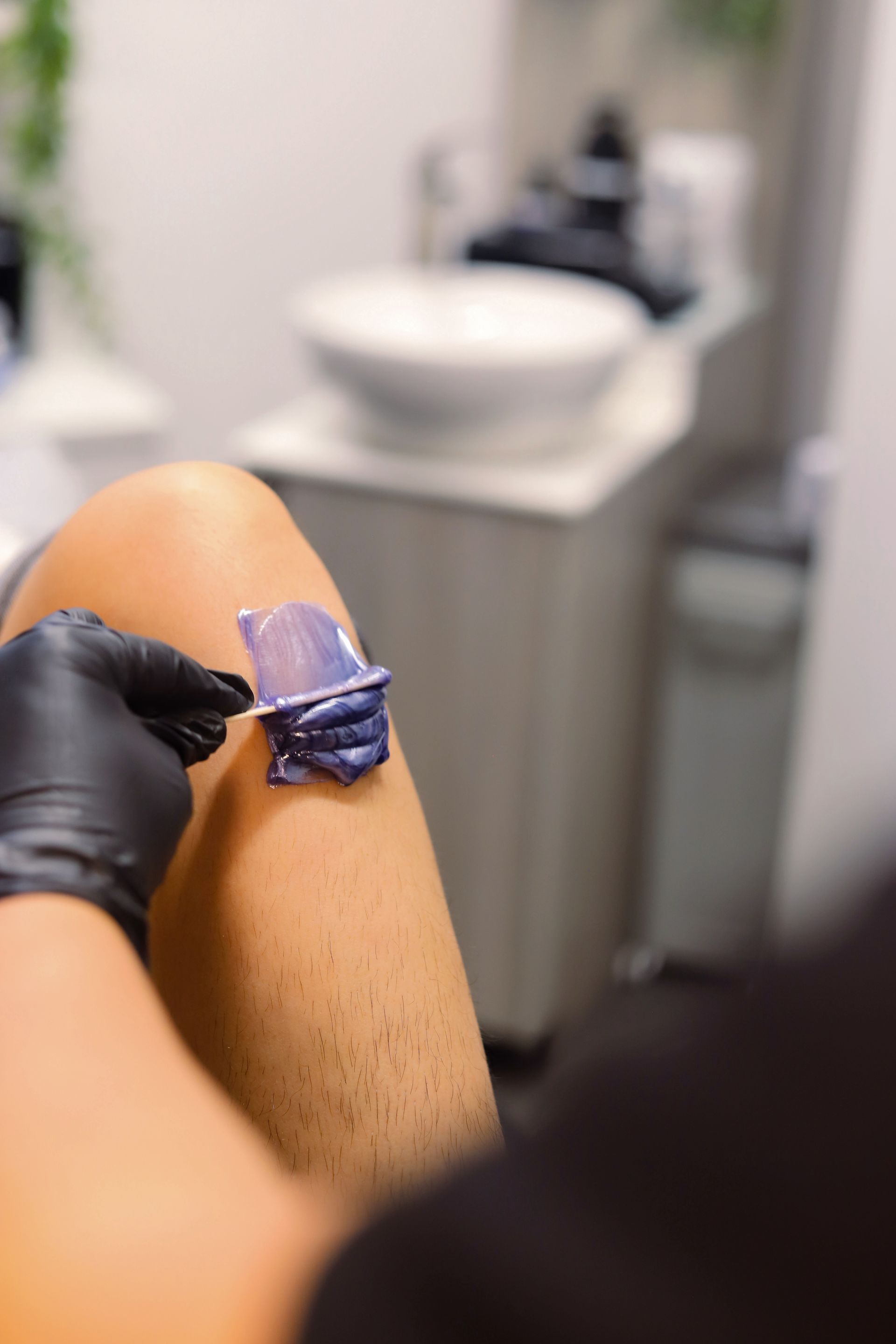 A person applying purple wax to a leg with a spatula, preparing for hair removal.