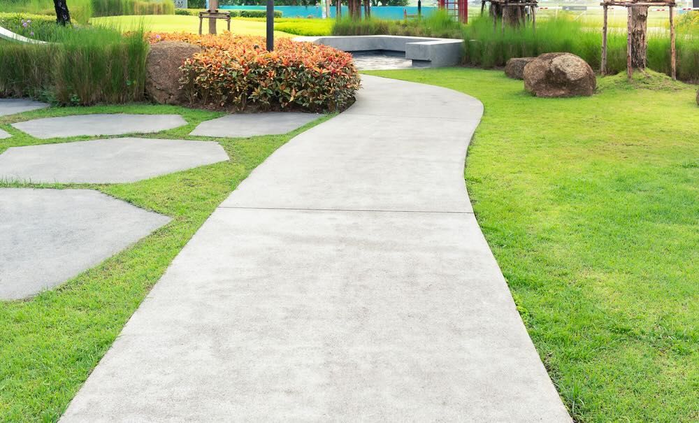 A concrete walkway in a park surrounded by green grass.