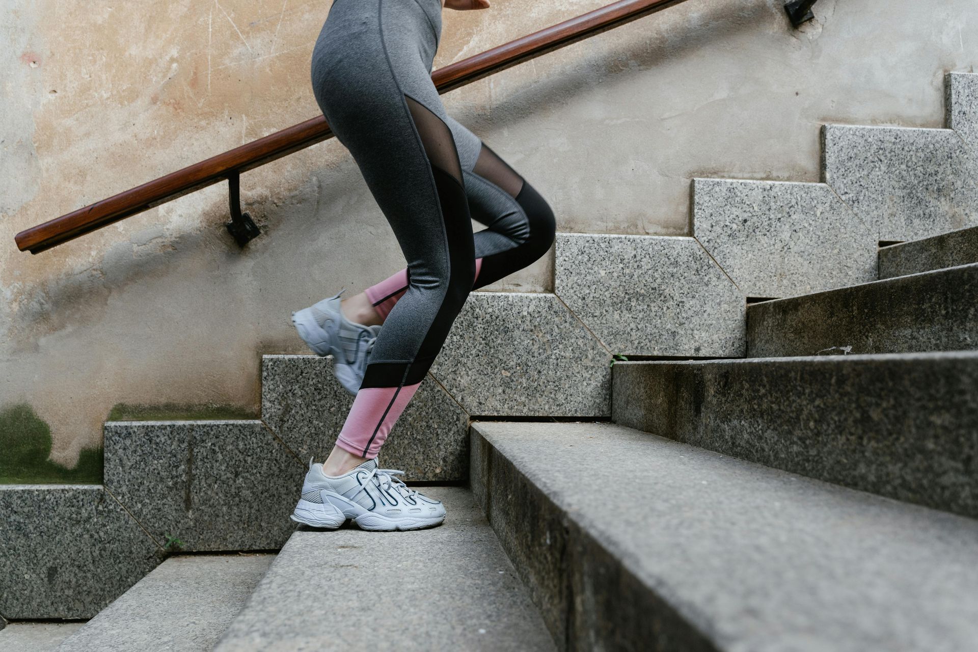 Person in gray leggings running up concrete stairs, hand on railing.