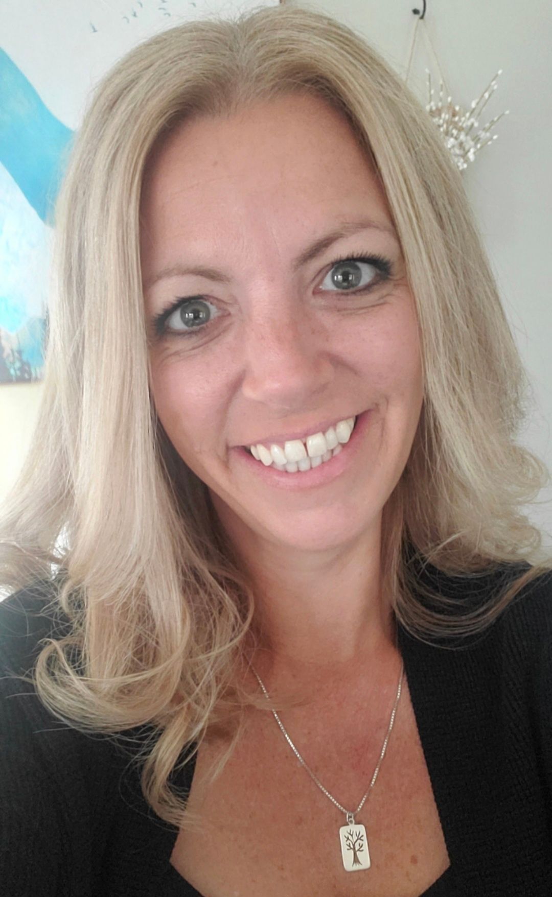 A woman with blonde hair is smiling and wearing a necklace.