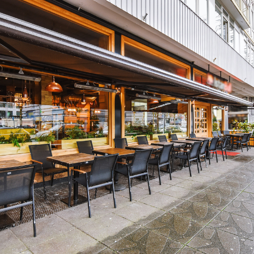 Outdoor restaurant seating under a retractable awning on a city sidewalk. Tables, chairs, and building facade.
