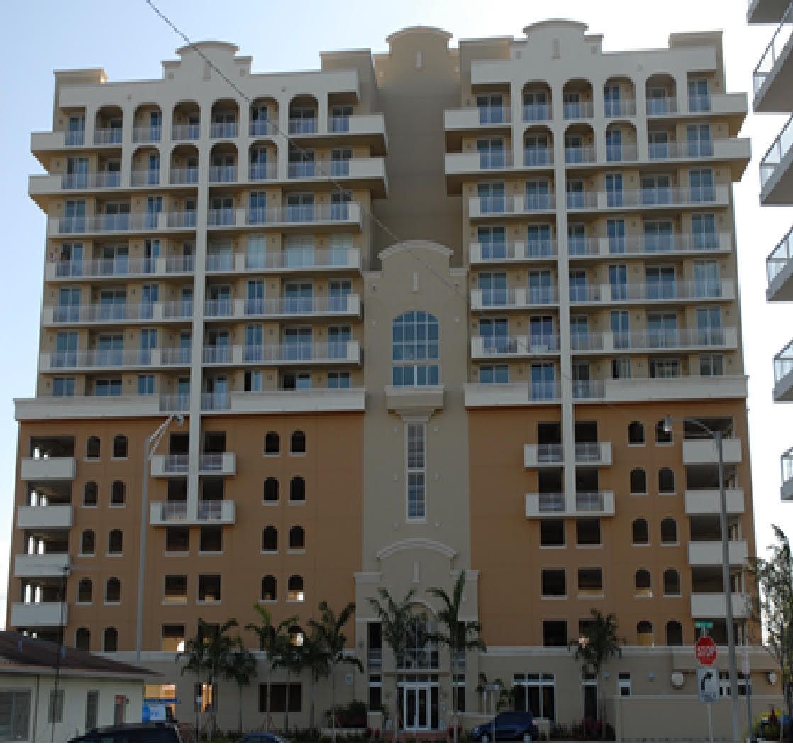 Man in black suit holding and using a tablet, smiling confidently. Gray background.