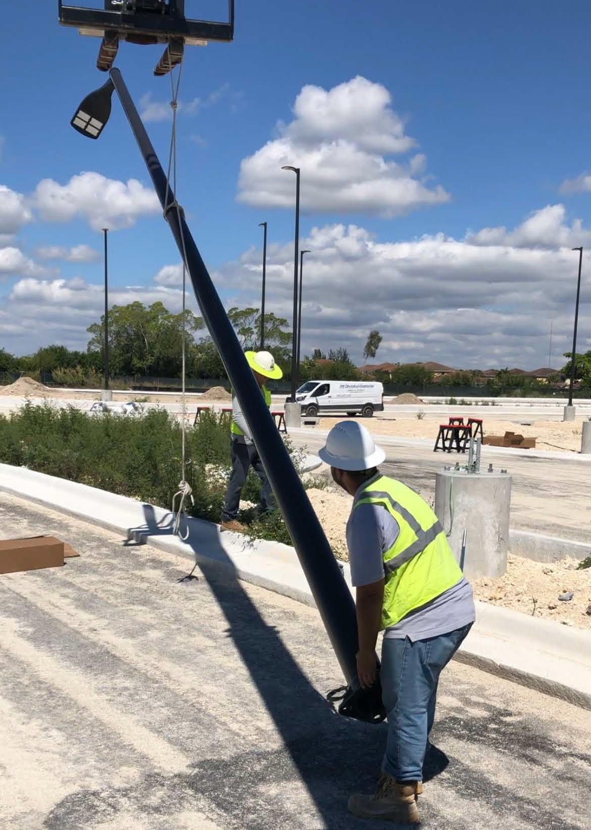 Engineer in safety vest and hard hat reviewing blueprints near a high-voltage power tower.