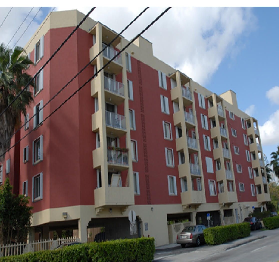 Electrical worker with arms crossed, smiling, wearing safety gear, in front of power lines.
