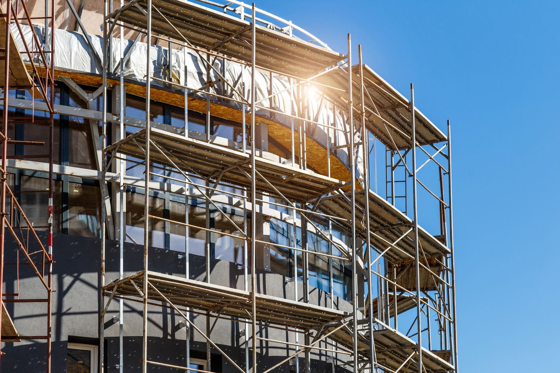 Scaffolding outside a commercial building under construction with su reflecting on the windows.