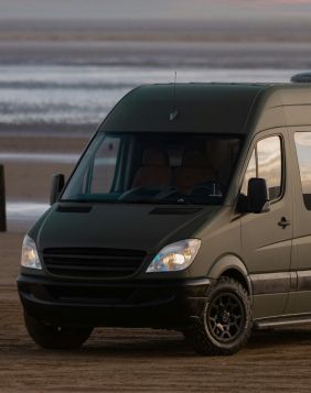 A matte olive green camper van parked on a sandy beach during sunset. | Suwanee Service Station