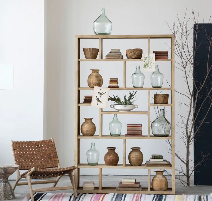 Wooden bookcase with decorative items, including vases and books, near a woven chair.