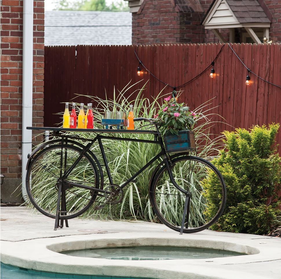 Decorative bicycle used as a bar, holding drinks and flowers, in a backyard setting.