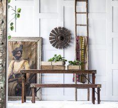 Wooden bench and table with decor: painting, plants, ladder, wall decoration.