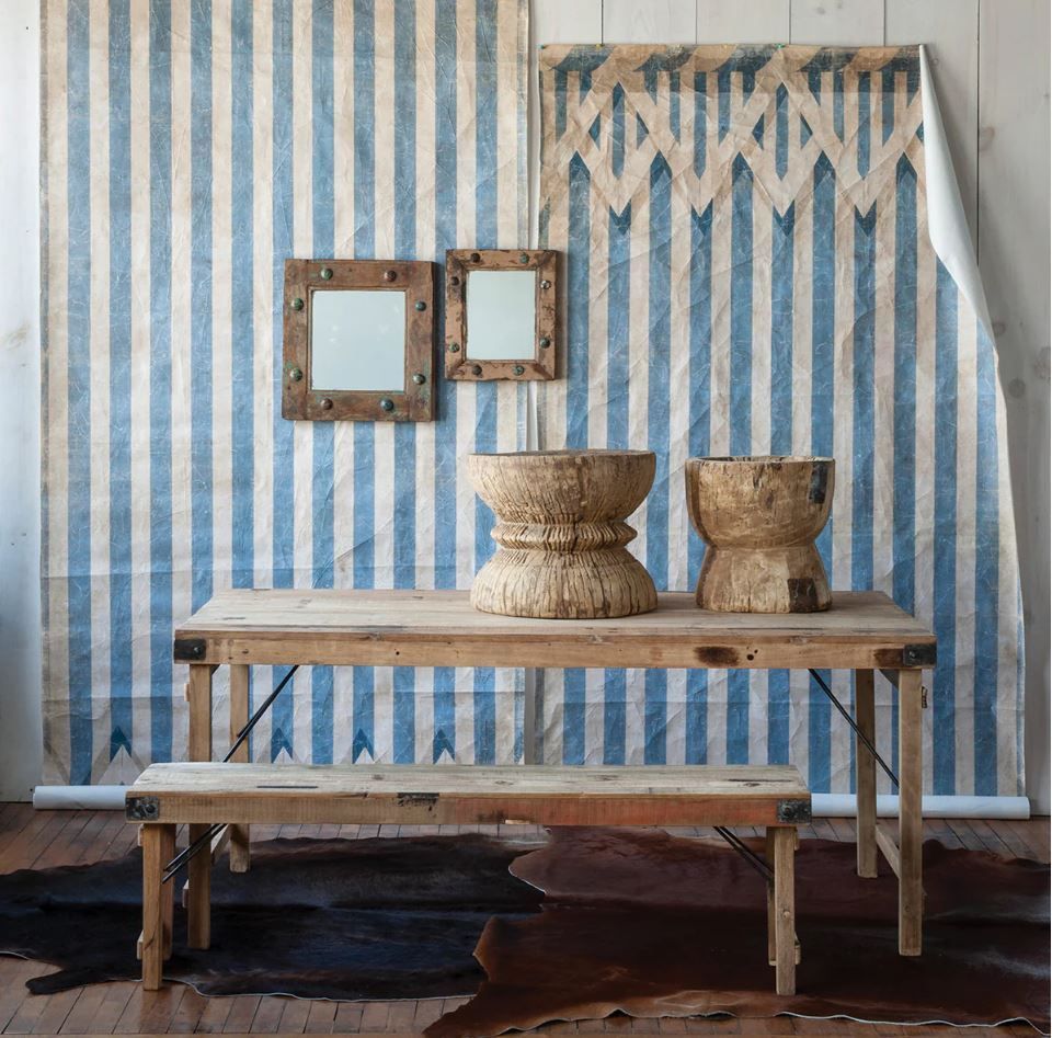 Rustic interior: wooden table and bench, blue and white striped backdrop, mirrors, and wood accent pieces.