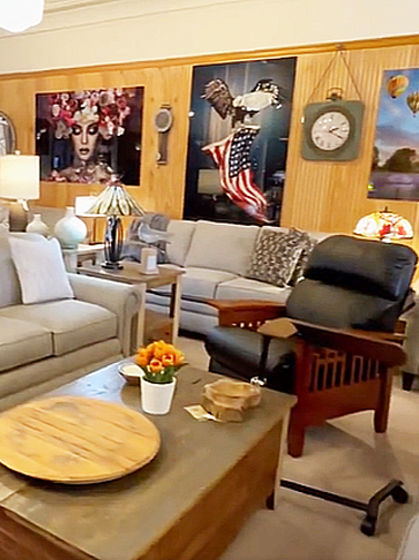 Furniture store interior with sofas, a recliner, coffee table, and artwork on wood-paneled walls.