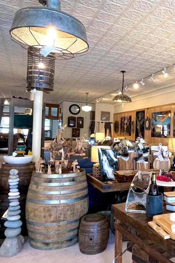 Shop interior with wooden barrels displaying artisan goods; overhead lighting, tin ceiling.