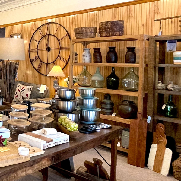 A rustic shop interior. Wooden shelving with bowls, glass jars, and a large clock on a wood-paneled wall.