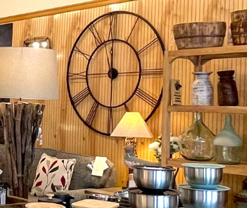 A rustic interior with a large clock, shelves of decor, and a sofa.
