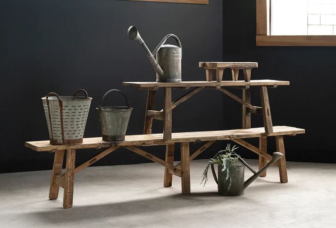 Wooden tiered bench with metal watering cans and buckets.