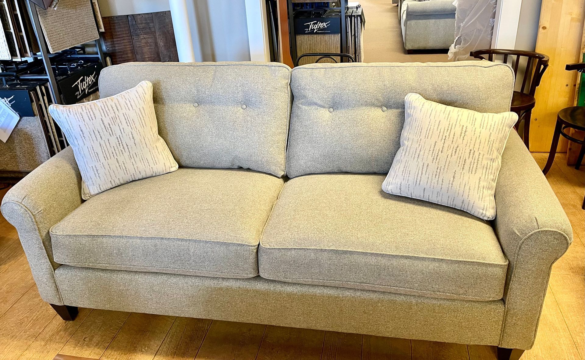 A light gray loveseat with two matching pillows, in a shop setting.