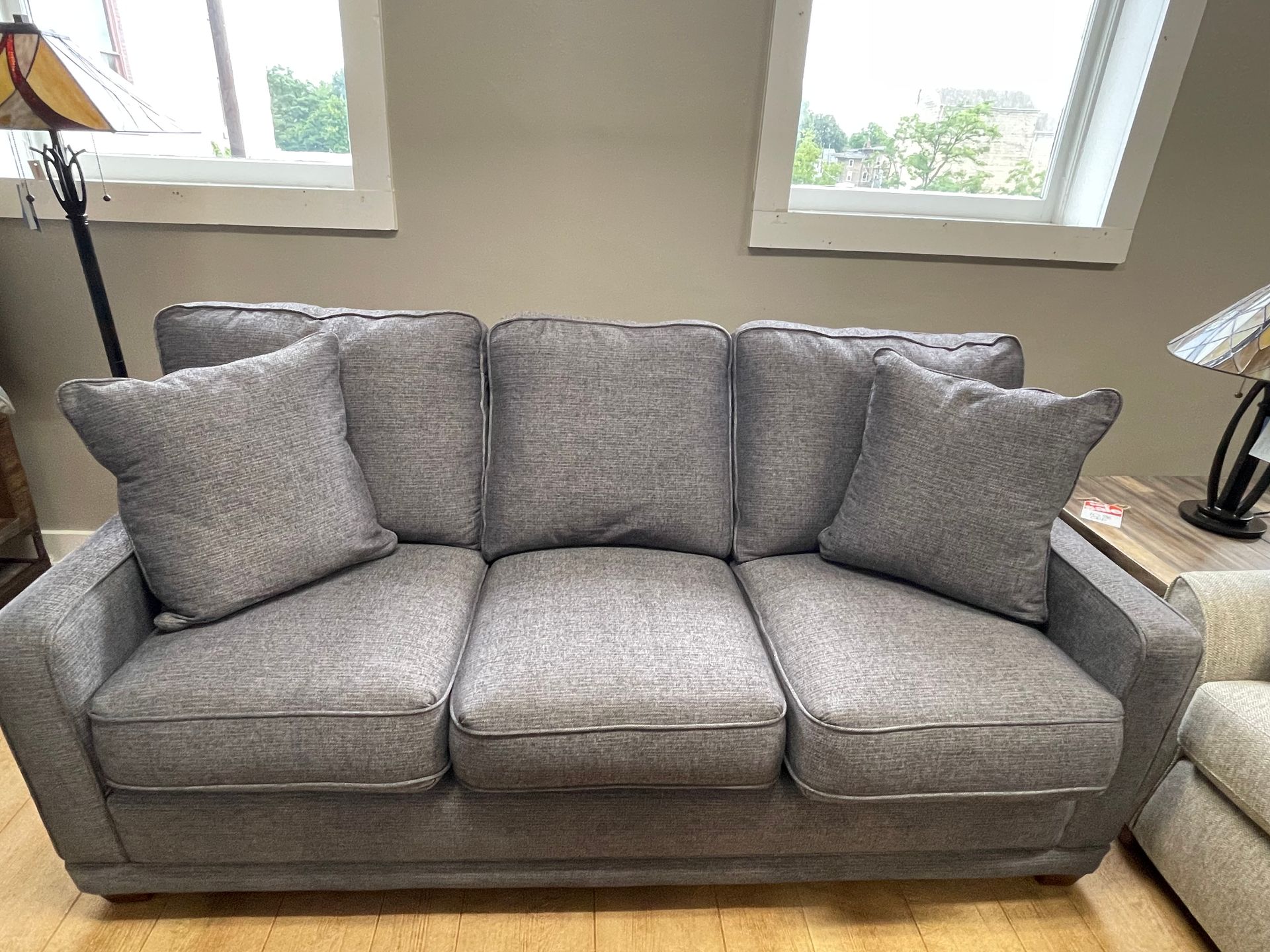 Gray fabric sofa with three seat cushions and two pillows, set in a room with windows.
