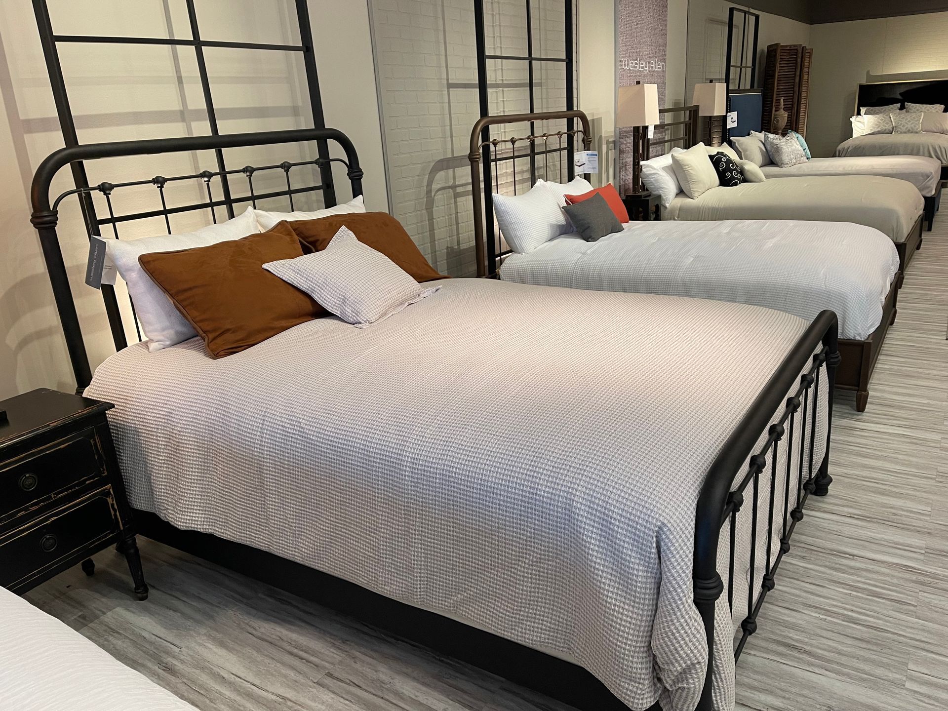 Several iron bed frames on display in a furniture store, with bedding and pillows.