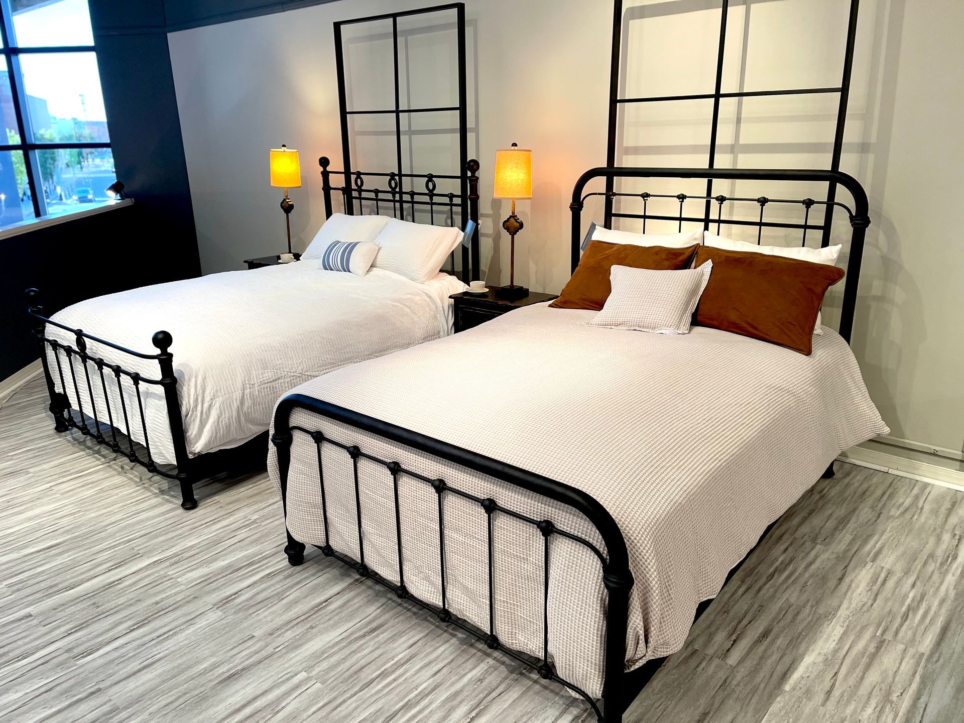Two beds with black frames, nightstands, lamps. Beige and white bedding, light colored rug.