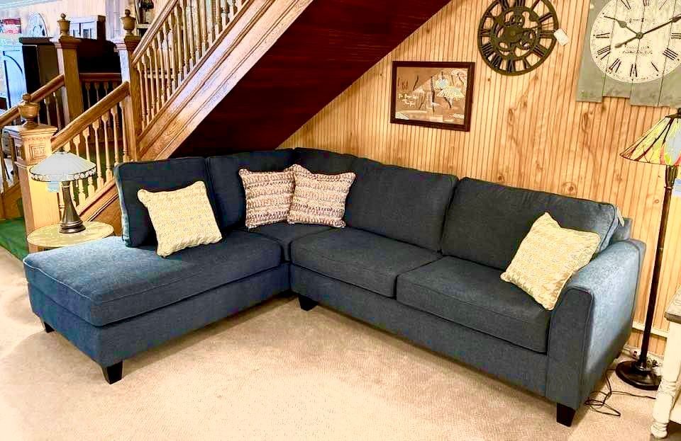 Blue sectional sofa with decorative pillows in a room with a wooden staircase.