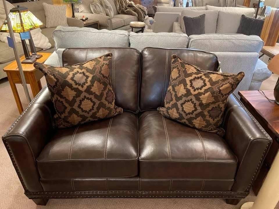 Leather loveseat with two decorative pillows in a furniture store.