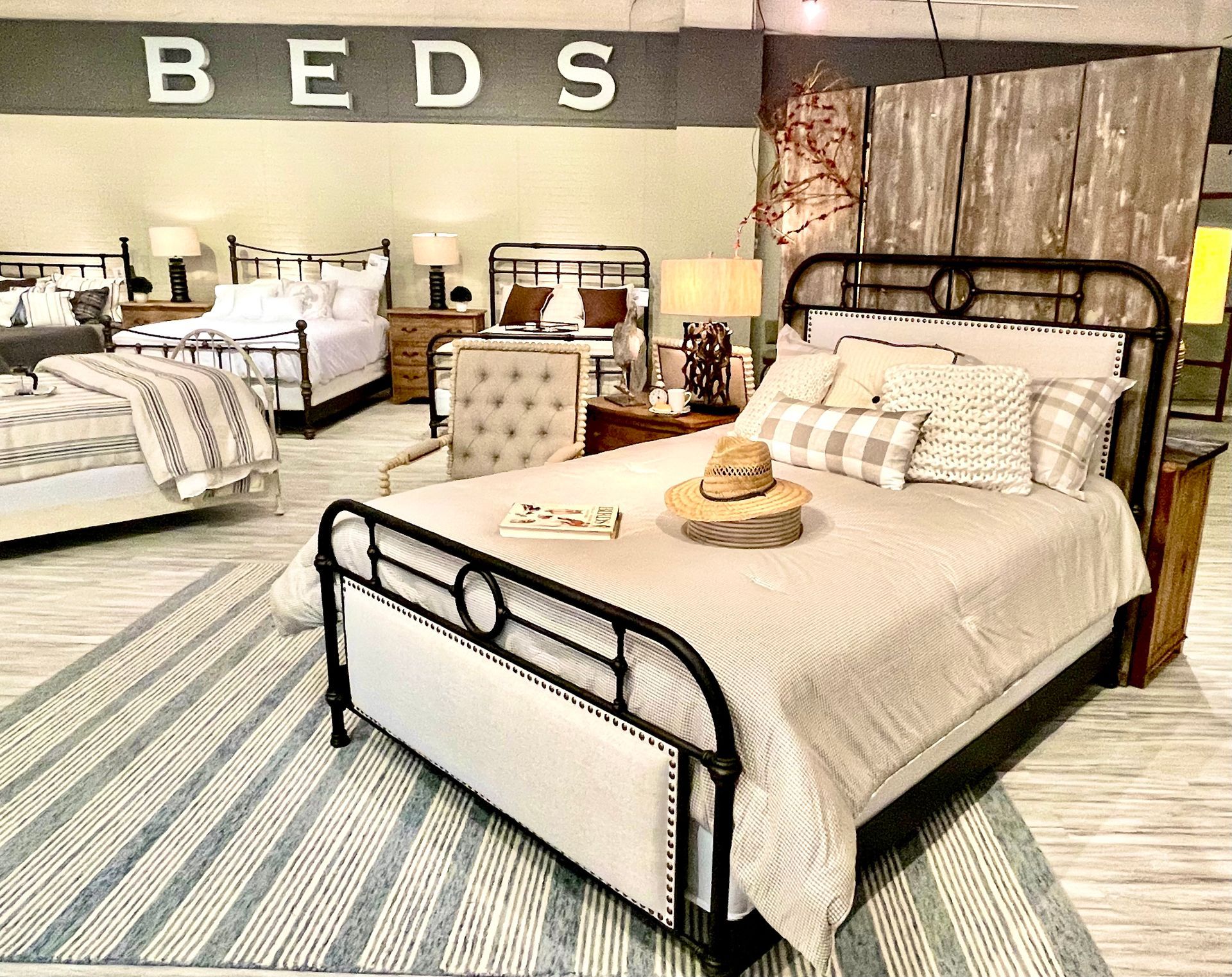 Beds displayed in a furniture store, featuring iron bed frames with bedding and decor. 