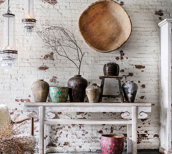 Rustic display: White brick wall backdrop with a white wooden console table. Various vases and a large woven basket.
