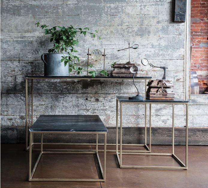 Three gold-framed tables with dark tops in front of a weathered gray wall, plants, and decor.