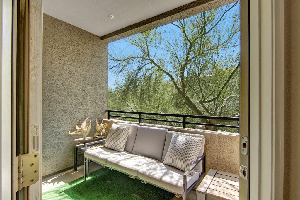 A balcony with a couch and a table and trees in the background.
