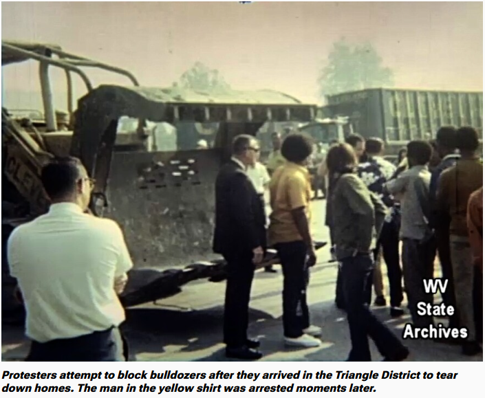 Protesters block bulldozers in the Triangle District. Man in yellow shirt arrested.