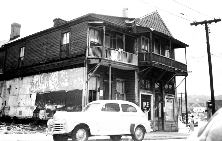Two-story wooden building with a balcony, a car parked in front.