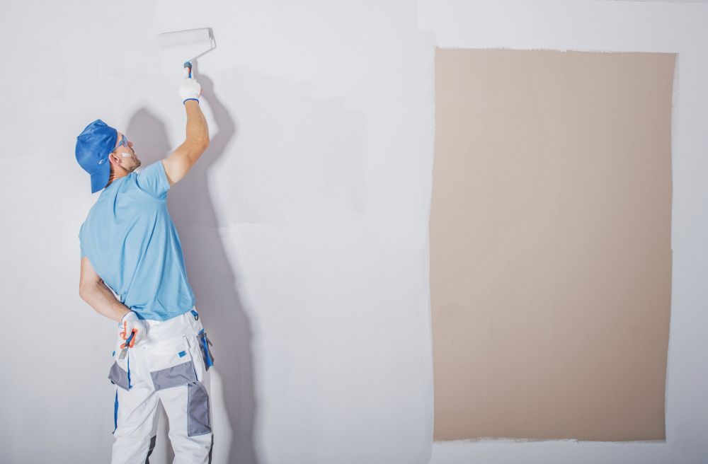 A Man Is Painting A Wall With A Paint Roller — Mid Coast Coatings In Kempsey, NSW