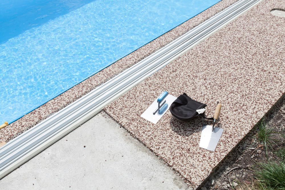 A Pair Of Trowel And A Bag Are Sitting On A Sidewalk Next To A Pool — Mid Coast Coatings In Kempsey, NSW