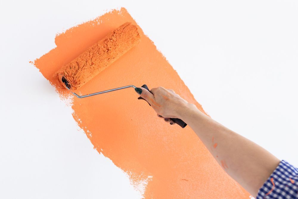 A Person Is Painting A Wall With An Orange Paint Roller — Mid Coast Coatings In Kempsey, NSW