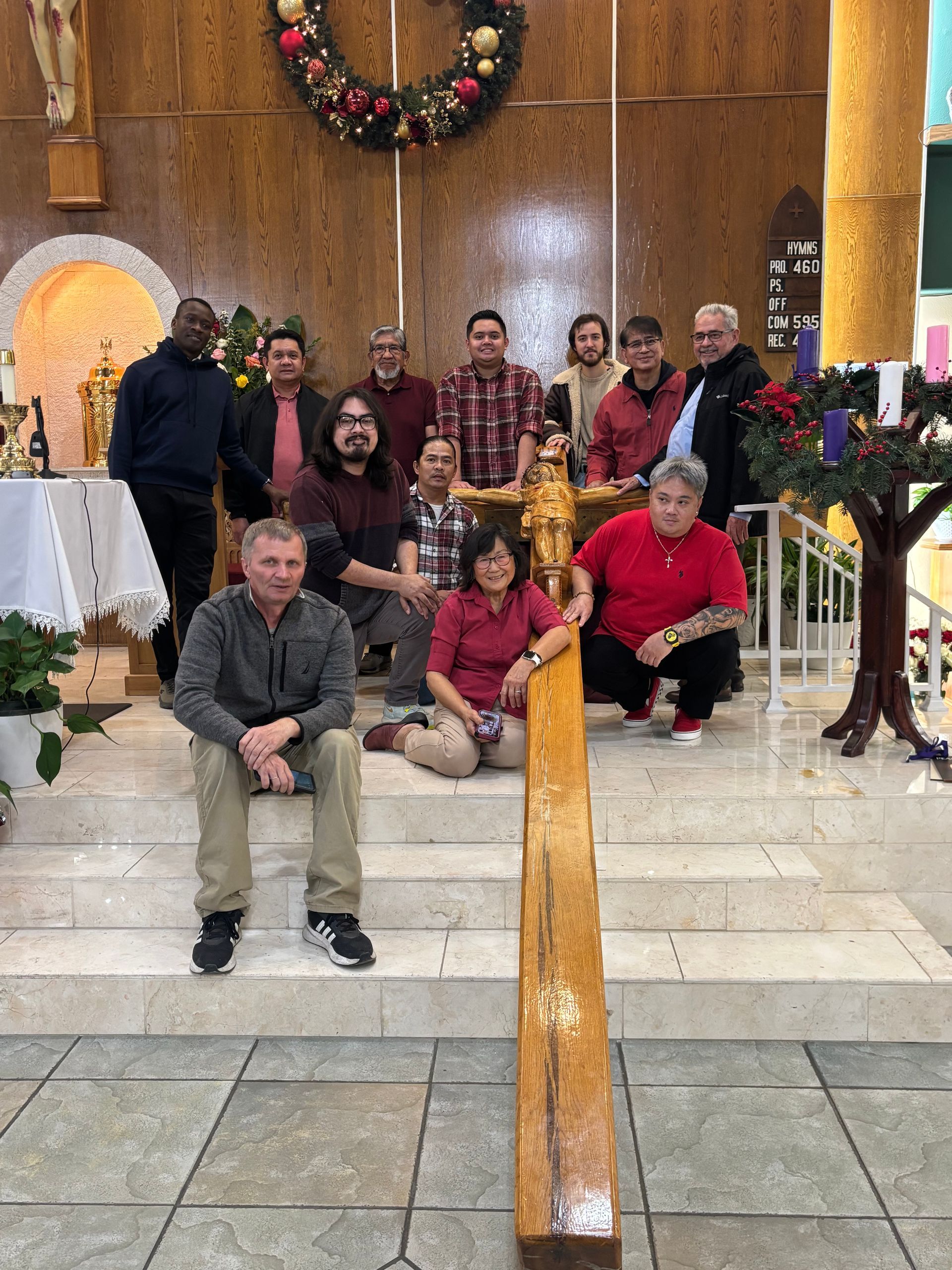 A group of people gathers in a church around a large wooden cross positioned on the altar steps.