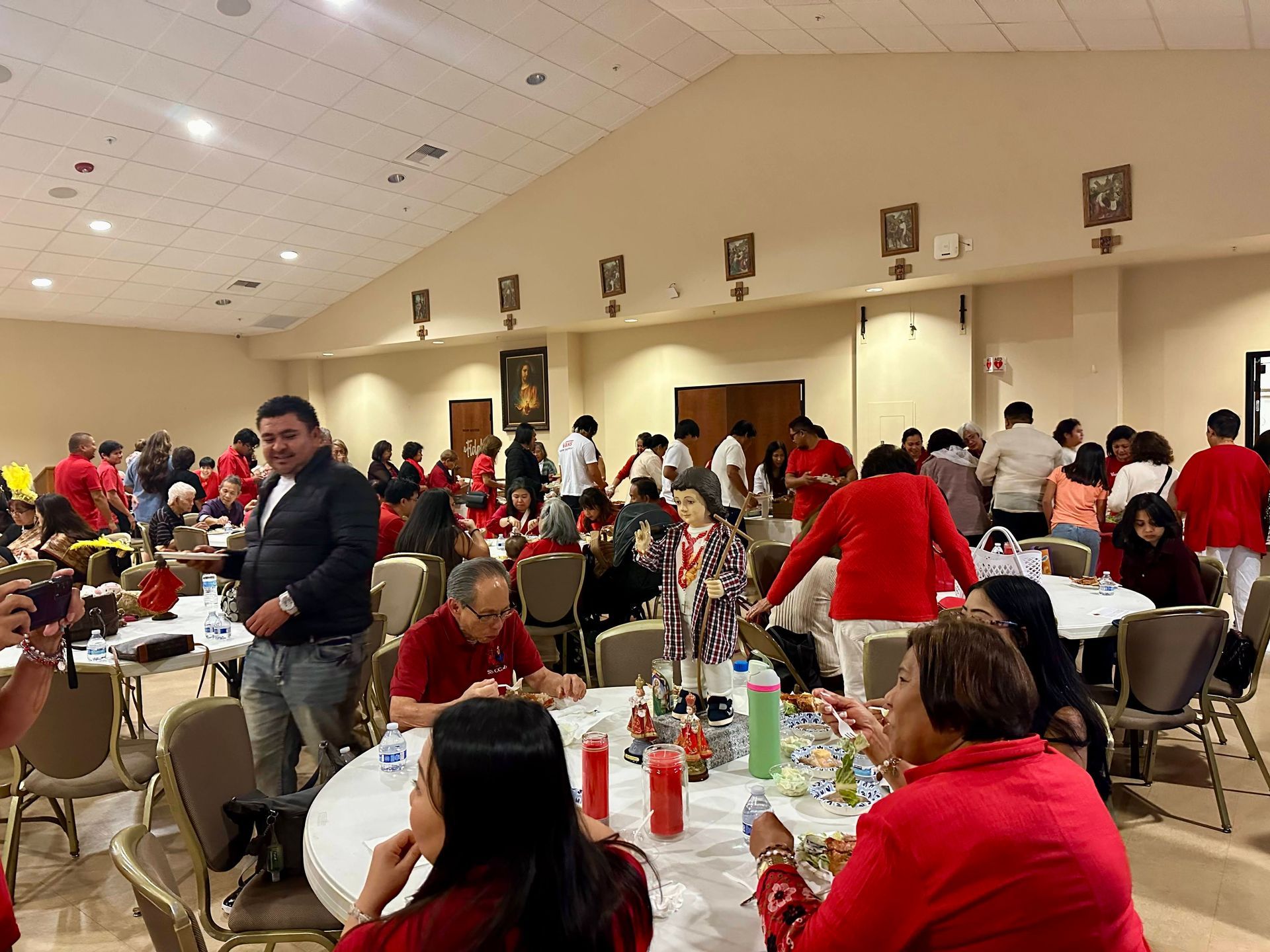 People wearing red at tables in a large hall, eating and socializing during a community gathering.