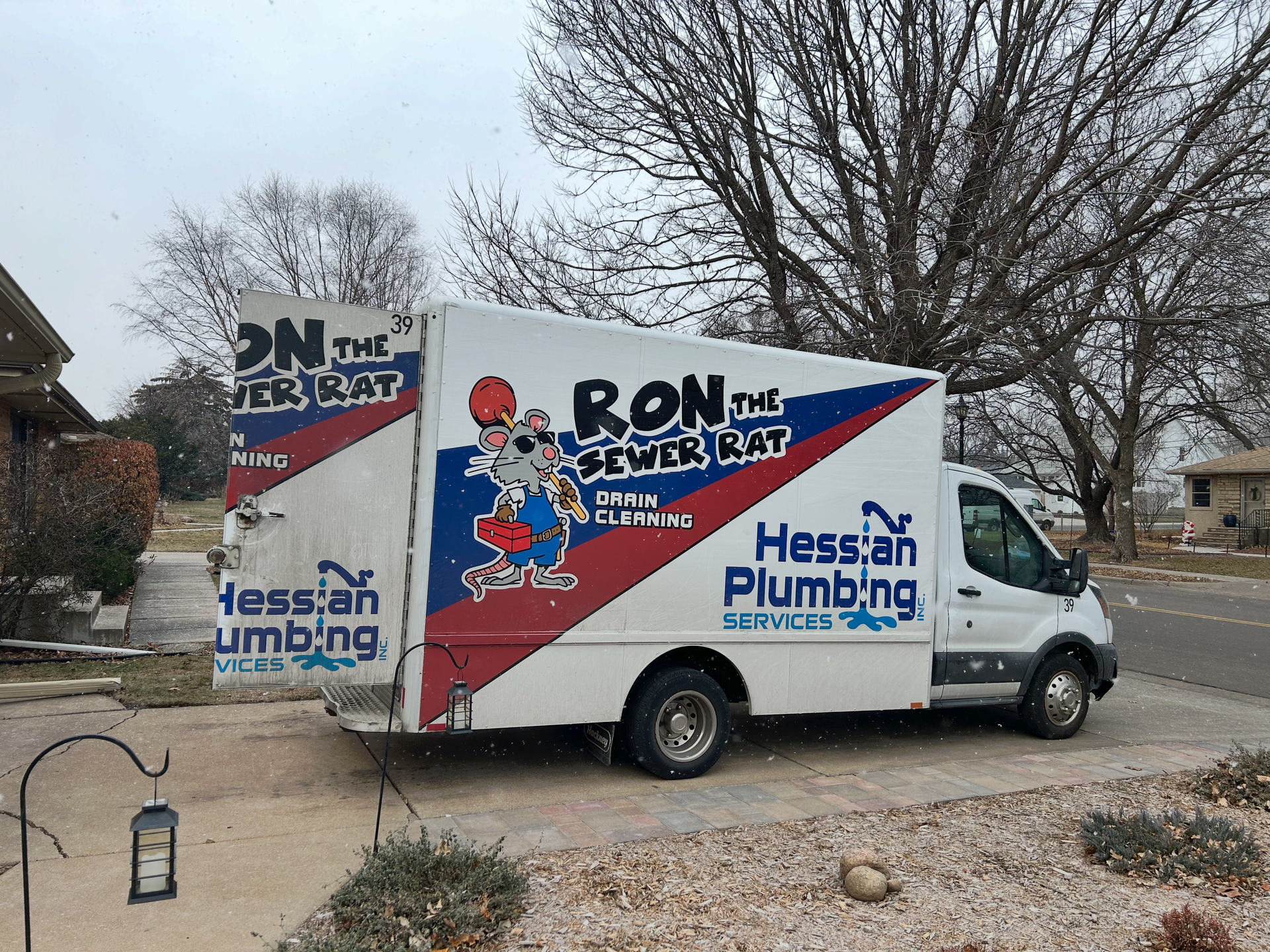 A white and blue JMR plumbing service van parked on a suburban street in front of a house.