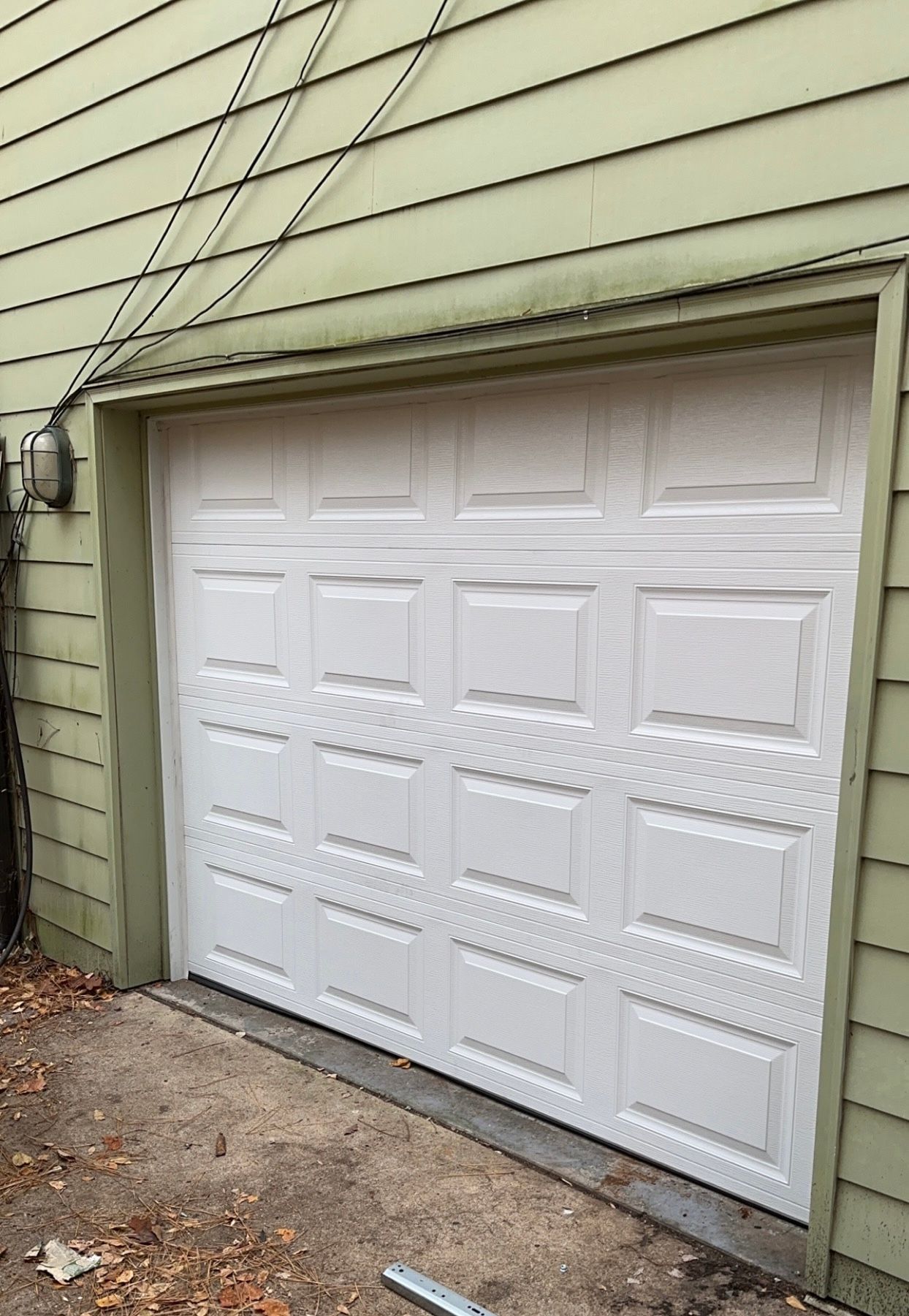 A white garage door is sitting in front of a green house.